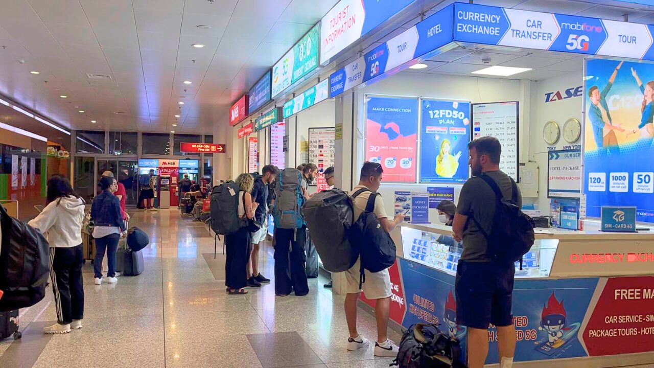 ノイバイ空港の国際線到着ロビーの様子。手前には人々がSIMカードを購入したり両替をしたりするためのカウンターの前に立っている。