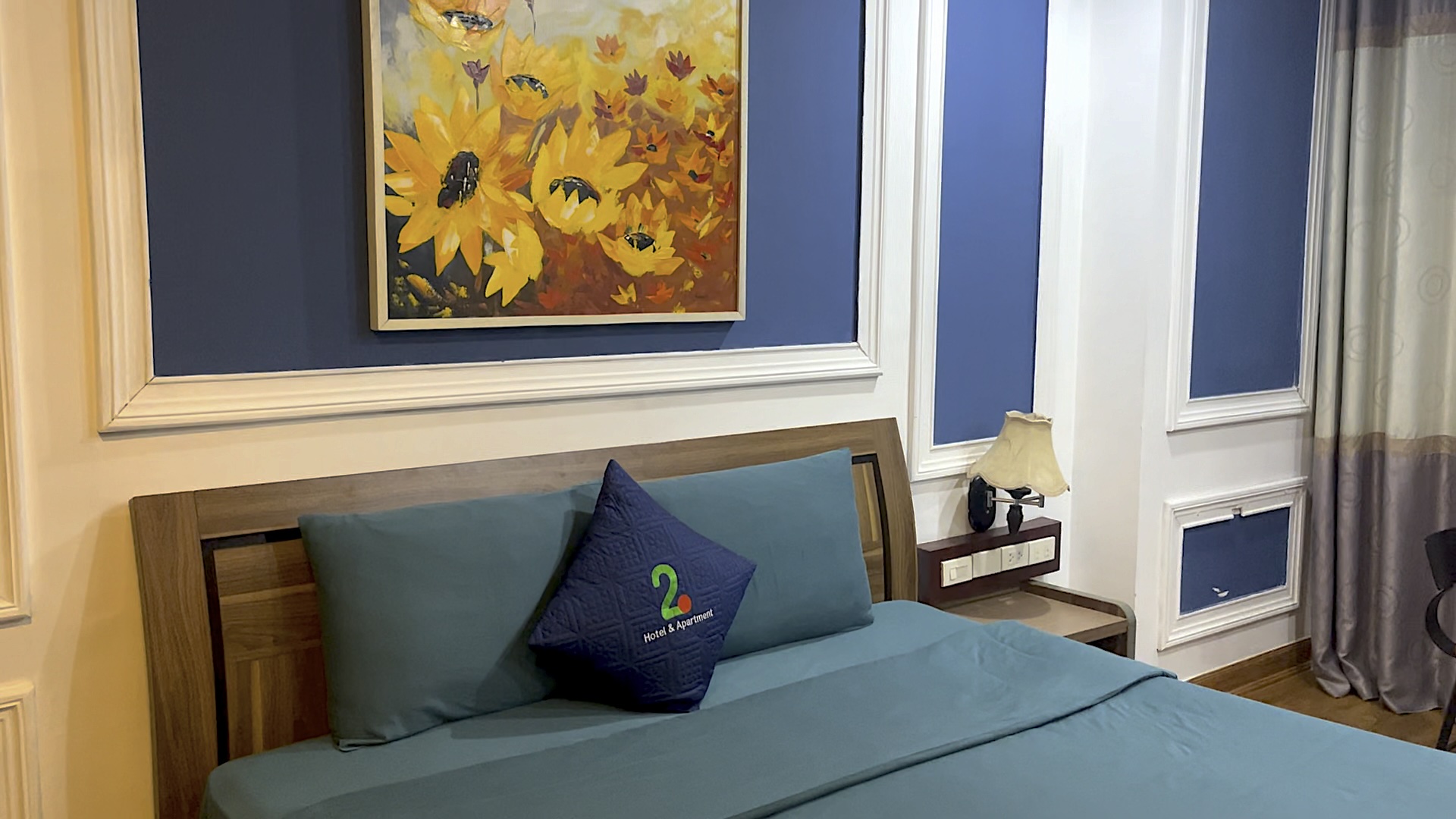 ハノイのホテルの部屋。緑色のシーツで覆われたベッドの上にはクッションが1つ置かれている。頭上にはひまわりの絵が飾られている。